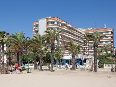 Mehrstöckiges Hotel mit Balkonen hinter Palmen an einem sonnigen Sandstrand.