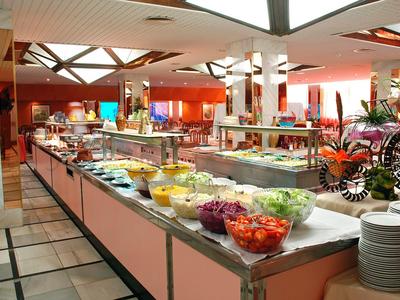 Buffet mit vielfältigen frischen Salaten und kalten Speisen in hellem Restaurant mit Pflanzen.