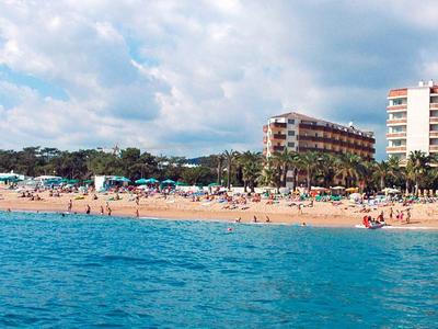 Strand mit hellgelbem Sand, blauen Meer, zahlreichen Menschen und hohen Gebäuden im Hintergrund.