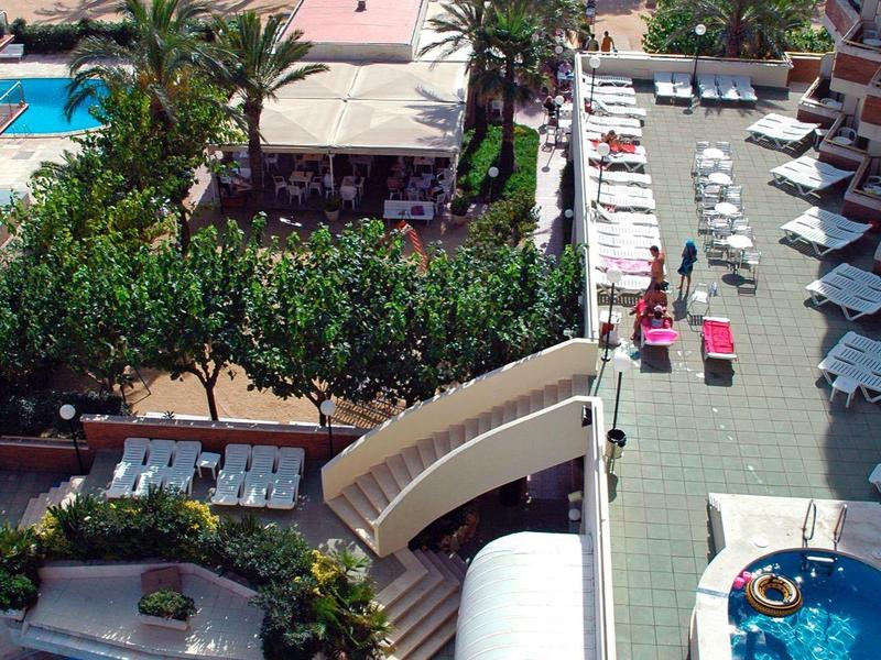 Blick von oben auf Poolanlage mit blauen Pools, Liegestühlen, Palmen und Strand im Hintergrund.