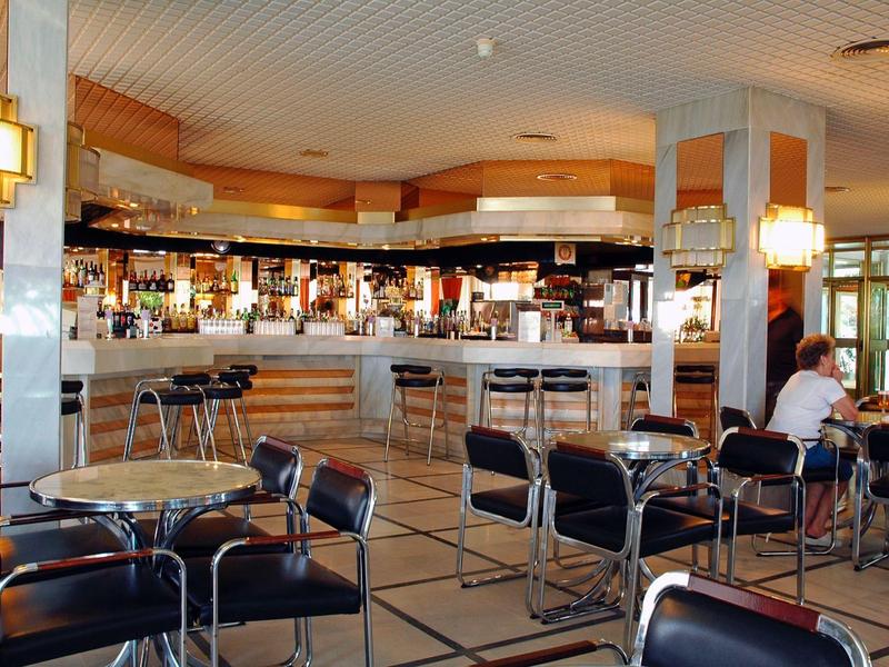 Modern eingerichtete Bar mit Theke, Hockern und Tischen mit schwarzen Stühlen in warmem Licht.