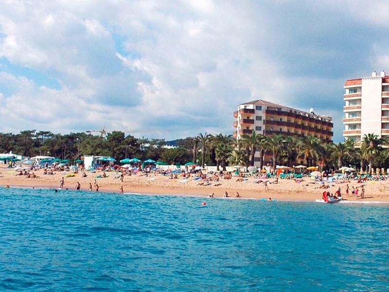 Strand mit hellgelbem Sand, blauen Meer, zahlreichen Menschen und hohen Gebäuden im Hintergrund.