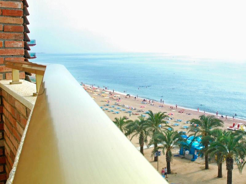 Balkon mit gelbem Geländer, Blick auf Strand, Meer und Palmen unter blauem Himmel.