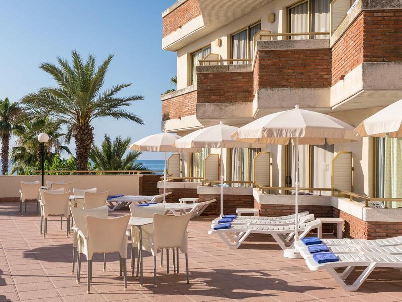 Terrassenbereich mit weißen Sonnenschirmen, Liegestühlen, Tischen und Stühlen, Palmen im Hintergrund.