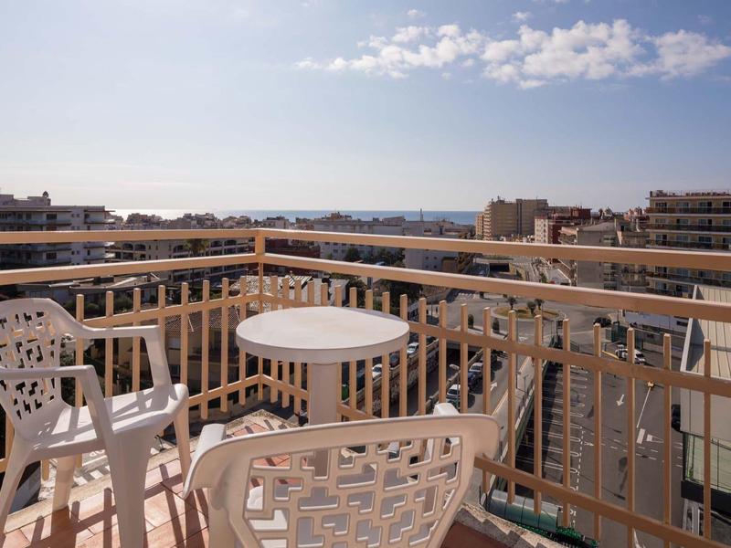 Balcón con mesa y sillas blancas, vista a la ciudad y el mar bajo cielo despejado.