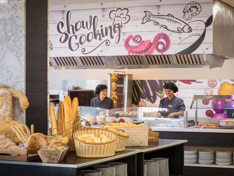 Panadería con diferentes tipos de pan, personal y decoración en la pared.