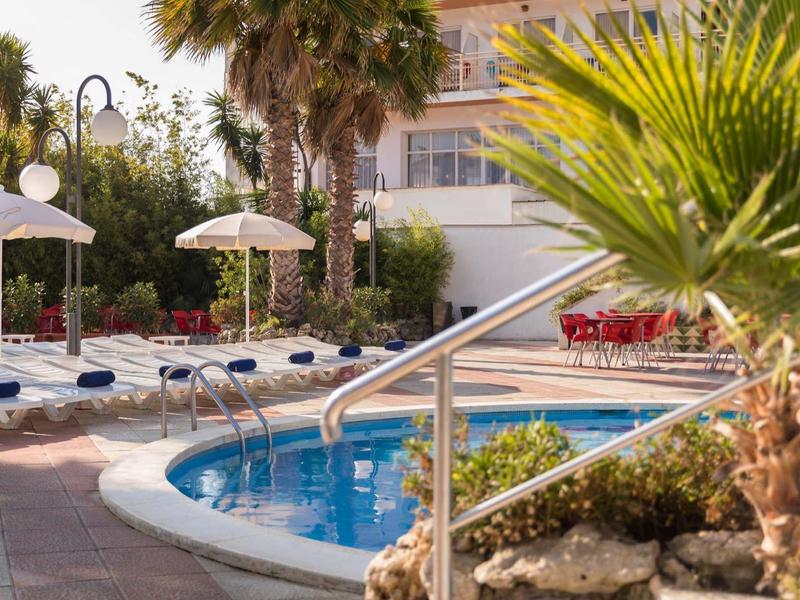 Área de piscina al aire libre con tumbonas, sombrillas y palmeras en un hotel.