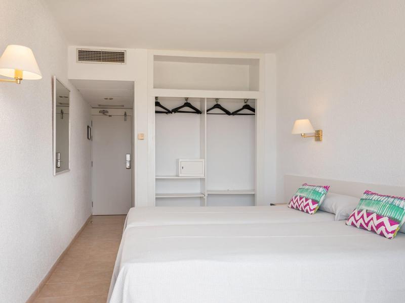 Habitación de hotel luminosa con dos camas, armario sin puertas y decoración minimalista.