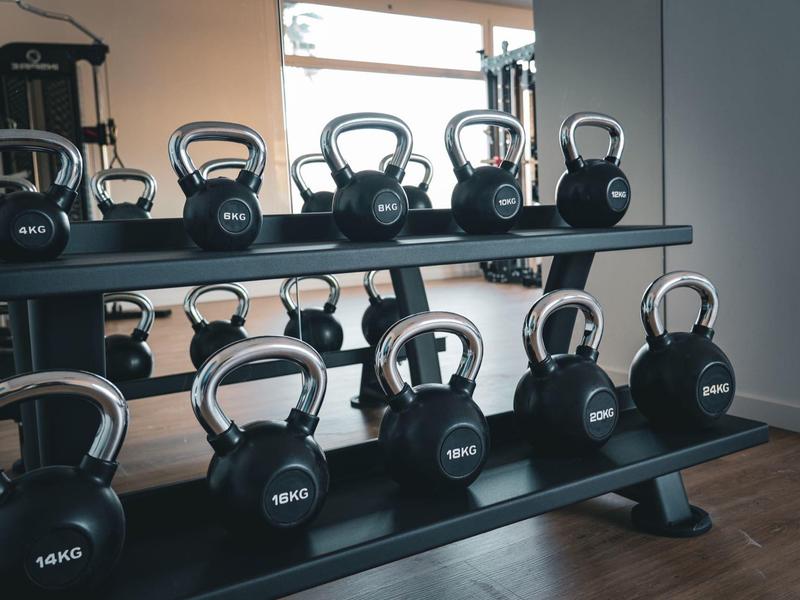 Dos filas de pesas rusas negras en un soporte gris frente a un espejo en el gimnasio.