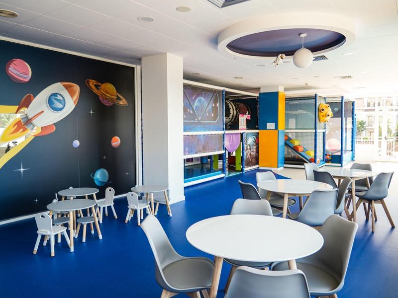 Área moderna y colorida para niños con mesas, sillas y decoración espacial.