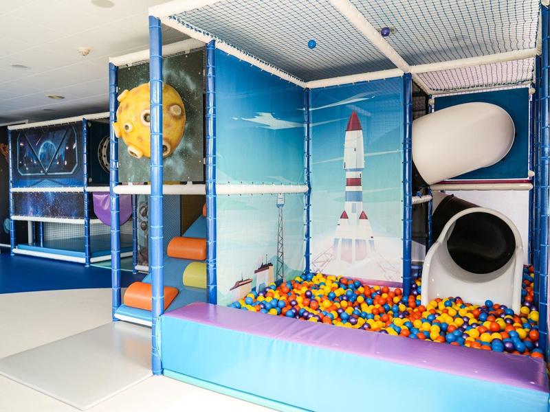 Área de juegos colorida para niños con piscina de bolas y toboganes en un espacio interior moderno.