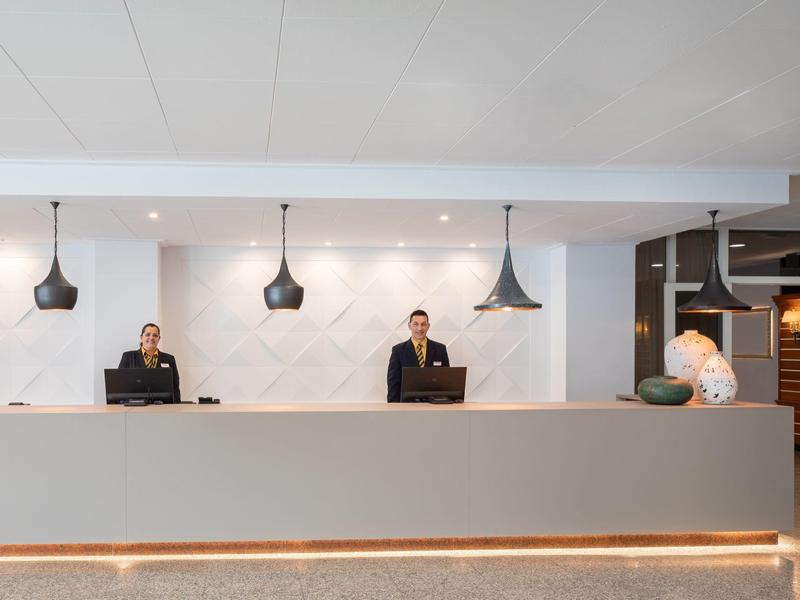 Área de recepción de hotel con dos empleados y iluminación moderna