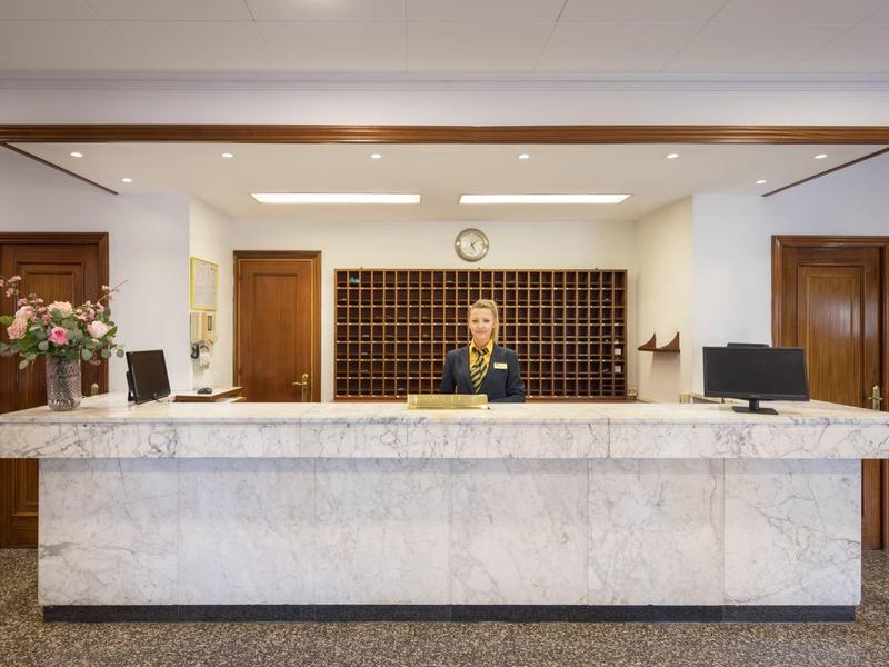 Recepcionista detrás de un gran mostrador de mármol en un área de recepción de hotel iluminada.