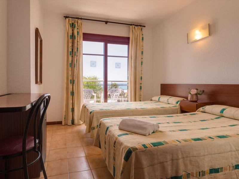 Habitación de hotel bien iluminada con dos camas individuales, escritorio y balcón con vista al exterior.