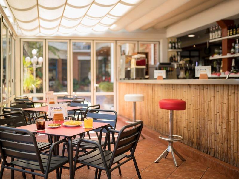 Acogedor bar del hotel con muebles de madera, taburetes y mesas bajo luz cálida.