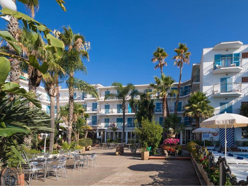 Hotel con piscina y tumbonas rodeado de palmeras y vegetación abundante