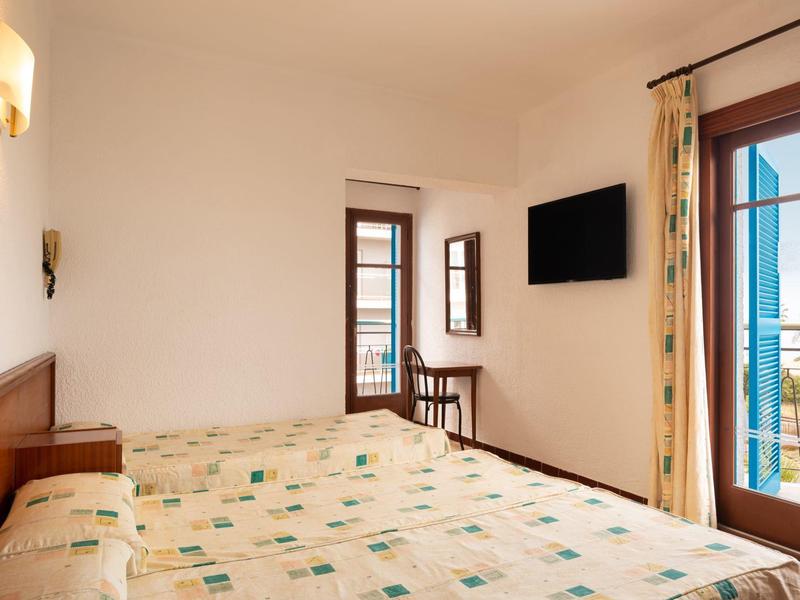 Habitación de hotel con cama doble, TV, ventana con vista a terraza y mar.
