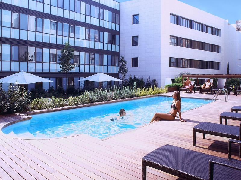 Modern outdoor area with blue pool, sun loungers, and guests at a hotel.