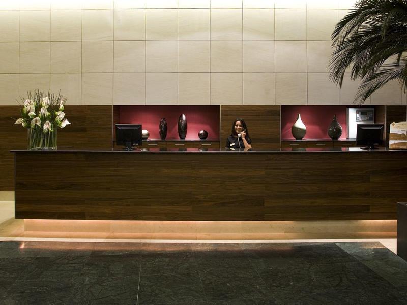 Modern hotel lobby reception with wooden desk, flower decor, and palm in an elegant setting.