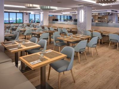 Restaurante moderno de hotel con suelo de madera y sillas acolchadas azules junto a mesas con cubiertos.