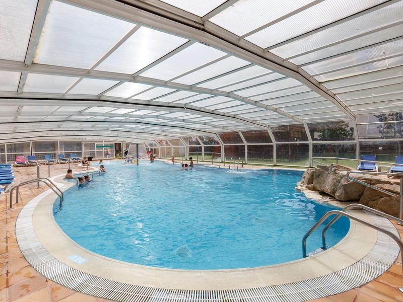Gran piscina cubierta con agua azul y techo acristalado en un hotel.