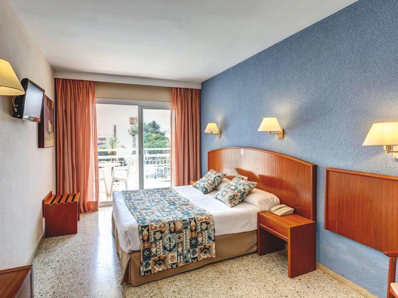 Habitación de hotel acogedora con cama doble, balcón y pared azul para estancias relajantes.