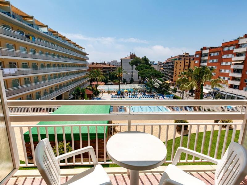 Vista desde un balcón con sillas y mesa hacia una piscina y edificios alrededor en un hotel.