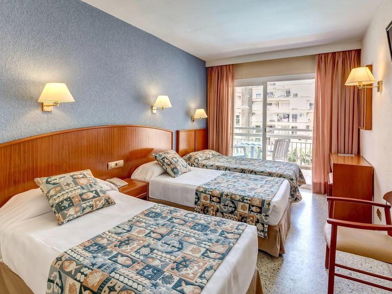 Habitación de hotel con dos camas individuales, muebles de madera, lámparas en la pared y balcón con vista exterior.