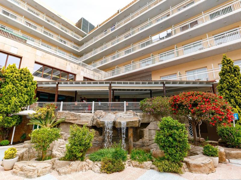 Edificio de hotel de varios pisos con un jardín cuidado y una cascada en el patio interior.