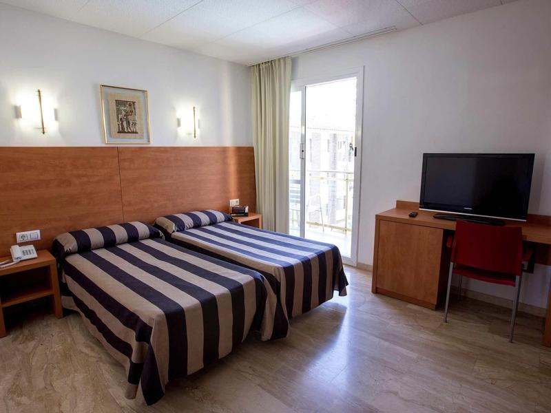 Camera d'hotel arredata semplicemente con due letti singoli, scrivania e TV.