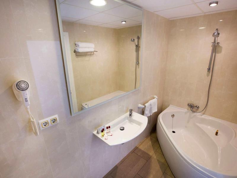 Bagno moderno con vasca, doccia, lavabo, grande specchio e asciugacapelli.