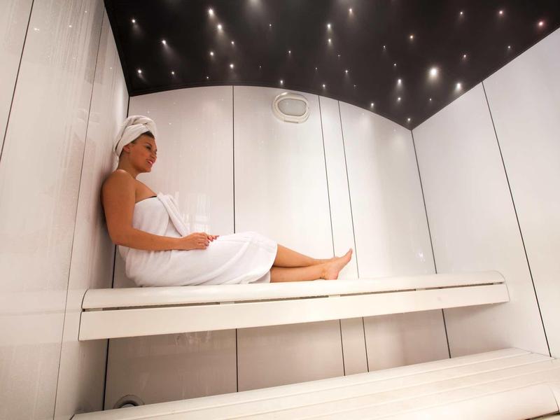 Donna rilassata in un bagno turco moderno con pareti bianche e soffitto scuro con luci.