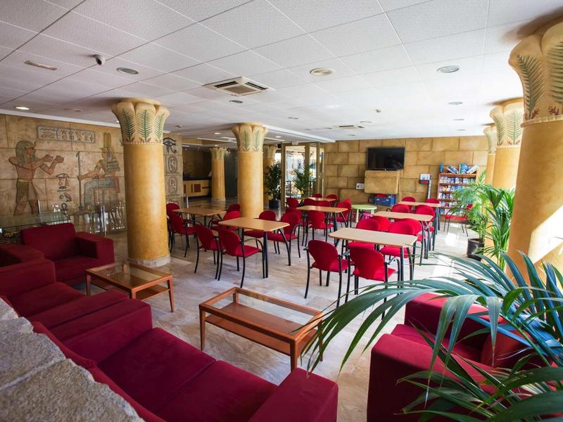 Spazio interno di un hotel accogliente con tavoli rossi e divani vicino a colonne e piante.