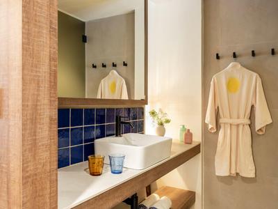 Modern bathroom with wooden shelf, white sink, blue tiled backsplash, and bathrobe.