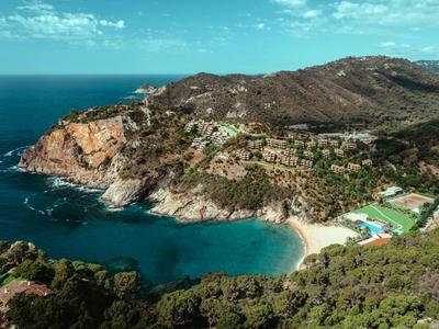 Panoramic view of a rocky coast with a hotel and beach nestled in green hills.
