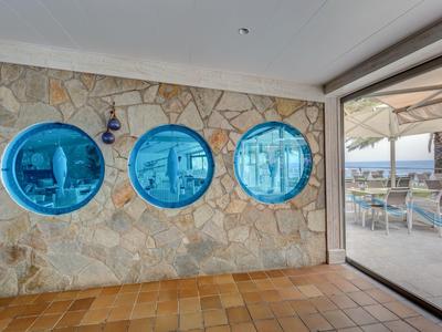 Three blue porthole windows in a stone wall overlooking a terrace and sea