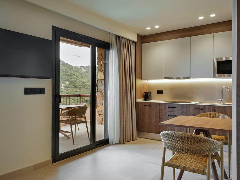 Modern kitchen area with wooden furniture and access to a balcony overlooking green hills.