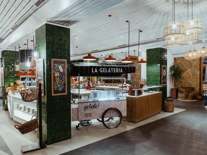 Modern gelato shop with cart, wooden counter, and chandeliers in a hotel restaurant.