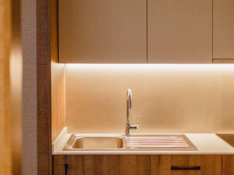 Modern kitchen sink area with wooden cabinets and indirect lighting.