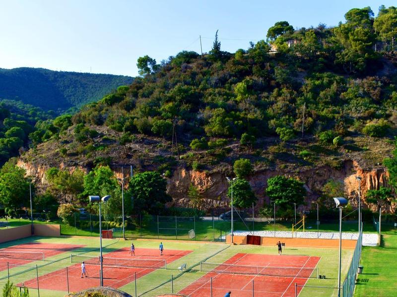 Several tennis courts in front of wooded hills and mountains under a clear sky.