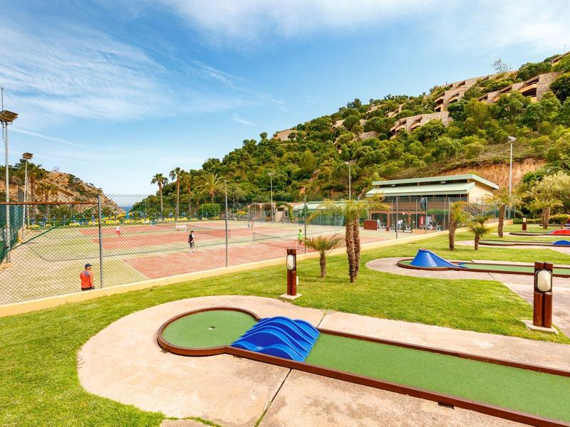 Outdoor putt-putt mini golf course with tennis courts and hills in the background.