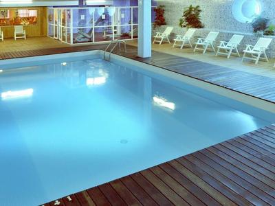 Binnenzwembad met houten vloer en witte stoelen langs de muur, verlicht in de avond