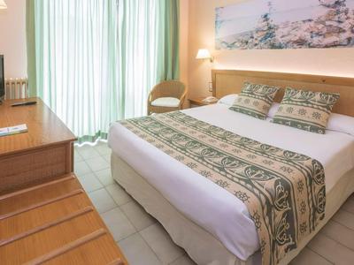 Licht ingerichte hotelkamer met tweepersoonsbed, bureau en balkon met daglicht.