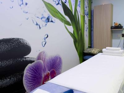 Behandelkamer met massagetafel, witte handdoeken en wanddecoratie met stenen en bloem.