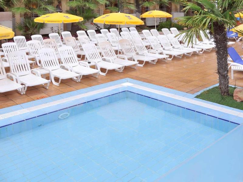 Klein zwembad met witte ligstoelen en gele parasols langs de rand.