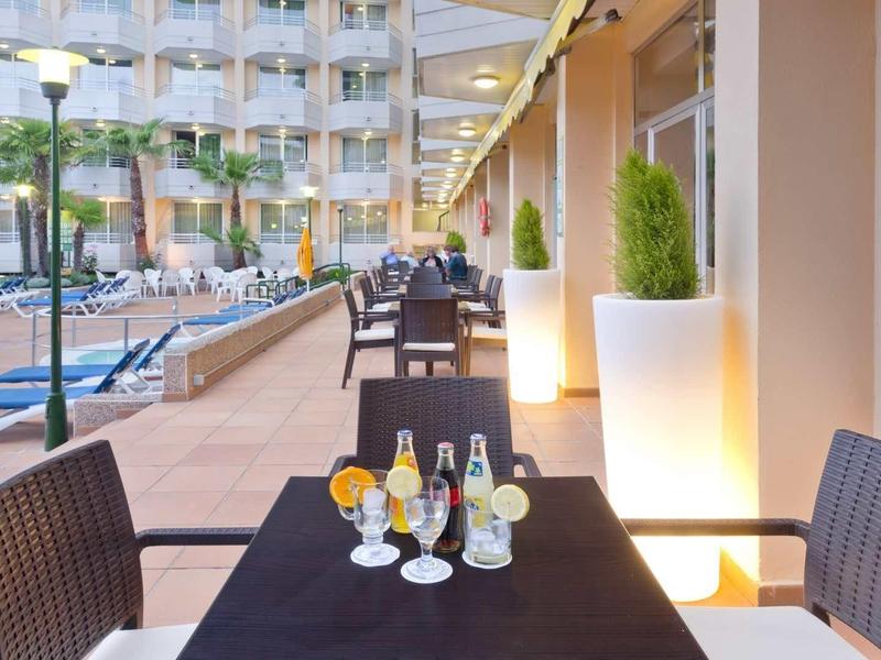 Terras met tafels en stoelen naast een zwembad voor een hotelgebouw.