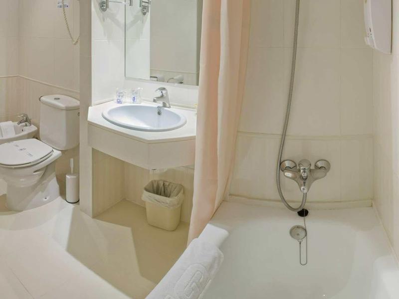 Lichte badkamer met wastafel, toilet, bidet en badkuip met gordijn.