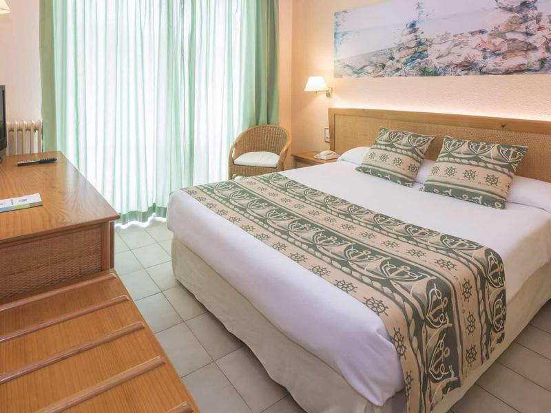 Licht ingerichte hotelkamer met tweepersoonsbed, bureau en balkon met daglicht.