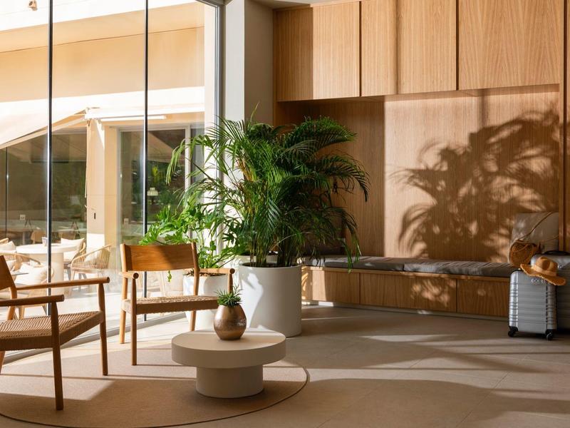 Habitación de hotel moderna con revestimiento de madera, plantas y gran ventanal hacia la terraza.