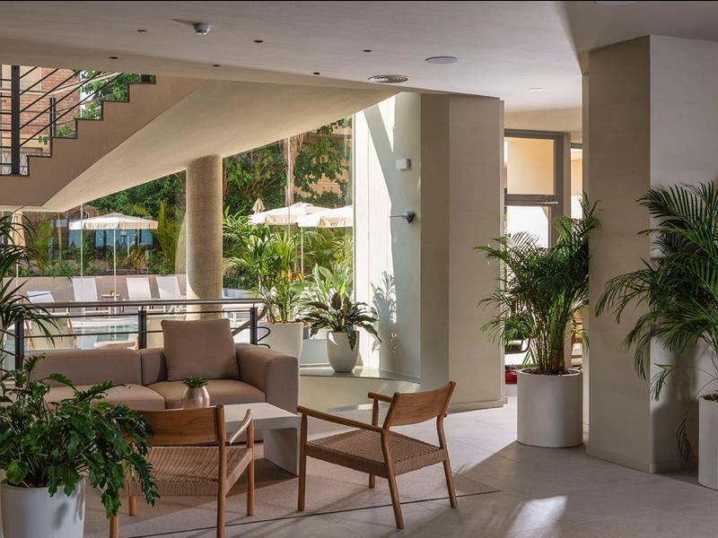 Lobby moderna de hotel con asientos, plantas y vista a la zona de piscina al aire libre.